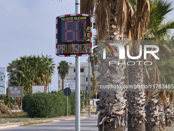 A solar-powered speed indicator installed along a palm-lined road aims to promote safe driving by monitoring and displaying vehicle speeds....