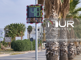 A solar-powered speed indicator installed along a palm-lined road aims to promote safe driving by monitoring and displaying vehicle speeds....