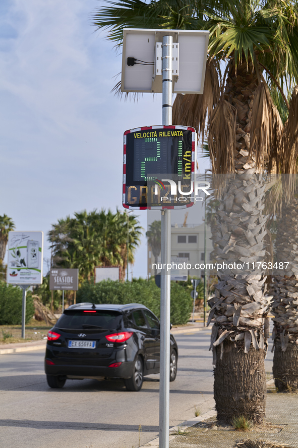 A solar-powered speed indicator installed along a palm-lined road aims to promote safe driving by monitoring and displaying vehicle speeds....