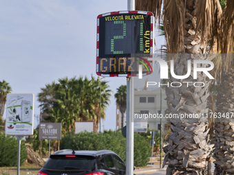 A solar-powered speed indicator installed along a palm-lined road aims to promote safe driving by monitoring and displaying vehicle speeds....