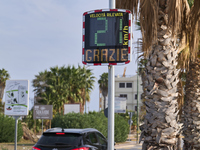 A solar-powered speed indicator installed along a palm-lined road aims to promote safe driving by monitoring and displaying vehicle speeds....