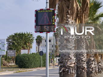 A solar-powered speed indicator installed along a palm-lined road aims to promote safe driving by monitoring and displaying vehicle speeds....