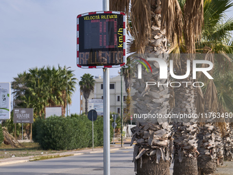 A solar-powered speed indicator installed along a palm-lined road aims to promote safe driving by monitoring and displaying vehicle speeds....