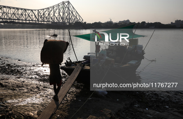 A laborer carries consumer goods to load onto a supply boat on the banks of the river Ganges at a wholesale market in Kolkata, India, on Nov...