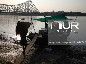 A laborer carries consumer goods to load onto a supply boat on the banks of the river Ganges at a wholesale market in Kolkata, India, on Nov...