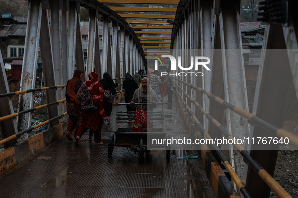 People walk on a bridge during rainfall on a winter day in Baramulla, Jammu and Kashmir, India, on November 11, 2024. 