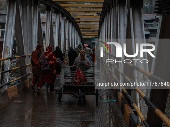 People walk on a bridge during rainfall on a winter day in Baramulla, Jammu and Kashmir, India, on November 11, 2024. (