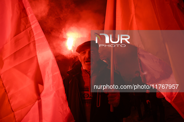 A man illuminated by flares holds Poland's national flag as he participates in the 106th anniversary of Poland regaining its independence in...