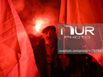 A man illuminated by flares holds Poland's national flag as he participates in the 106th anniversary of Poland regaining its independence in...