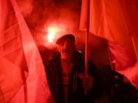 A man illuminated by flares holds Poland's national flag as he participates in the 106th anniversary of Poland regaining its independence in...