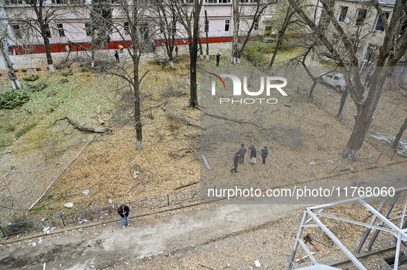 People stand among broken tree branches outside a hostel where internally displaced persons live, which is damaged by an overnight Russian a...