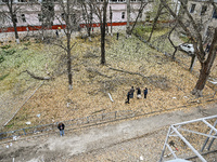 People stand among broken tree branches outside a hostel where internally displaced persons live, which is damaged by an overnight Russian a...