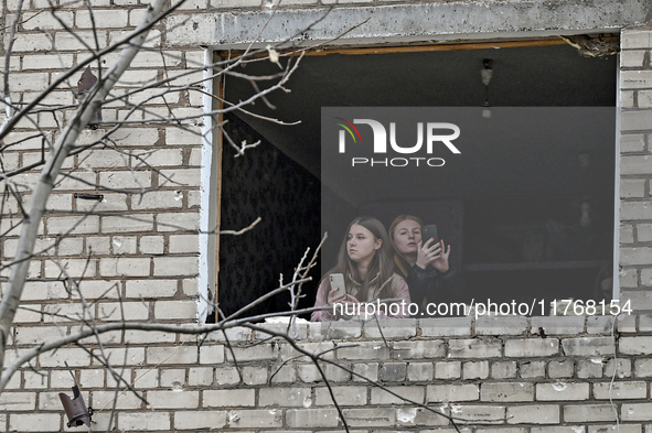 Two women look out of a window knocked out by a shock wave in a room of a hostel where internally displaced persons live, damaged by an over...