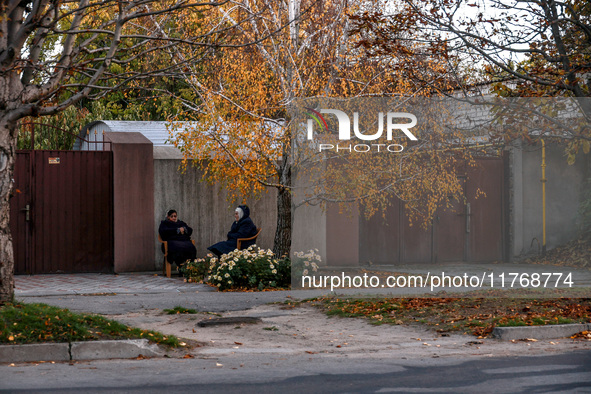 Women sit in plastic chairs in the street by the fence in Kherson, Ukraine, on November 7, 2024. 