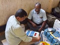 Polling officials check Electronic Voting Machines (EVMs) and other polling materials after receiving them from a distribution center on the...