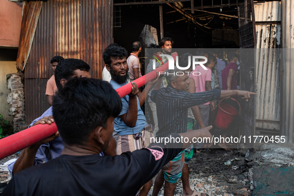 Local people help with the water pipe of the fire service to extinguish the fire at a shoe factory in the Shyampur area in Dhaka, Bangladesh...