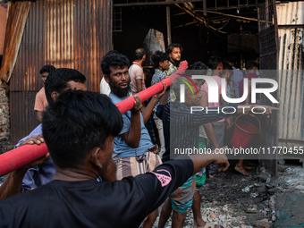 Local people help with the water pipe of the fire service to extinguish the fire at a shoe factory in the Shyampur area in Dhaka, Bangladesh...