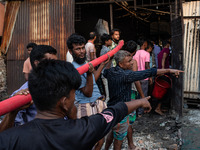 Local people help with the water pipe of the fire service to extinguish the fire at a shoe factory in the Shyampur area in Dhaka, Bangladesh...