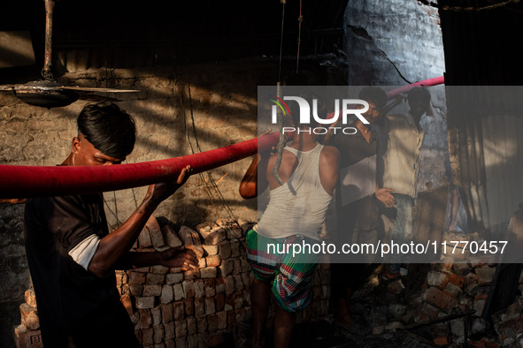 Local people help with the water pipe of the fire service to extinguish the fire at a shoe factory in the Shyampur area in Dhaka, Bangladesh...