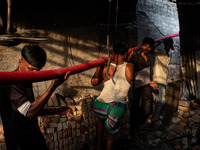 Local people help with the water pipe of the fire service to extinguish the fire at a shoe factory in the Shyampur area in Dhaka, Bangladesh...