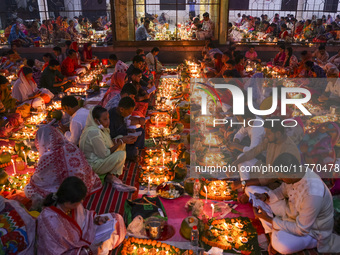 Hindu devotees sit together in front of oil lamps and candles and pray to Lokenath Brahmachari, a Hindu saint and philosopher, as they obser...