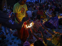 Hindu devotees sit together in front of oil lamps and candles and pray to Lokenath Brahmachari, a Hindu saint and philosopher, as they obser...