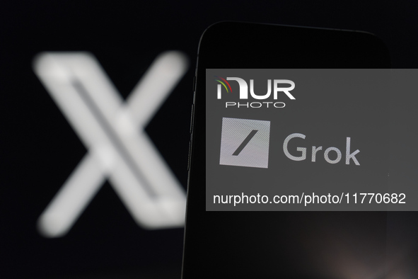 An iPhone displays the Grok AI chatbot icon, with the X platform icon visible on an iMac screen in the background. Grok, Elon Musk's AI chat...