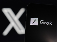 An iPhone displays the Grok AI chatbot icon, with the X platform icon visible on an iMac screen in the background. Grok, Elon Musk's AI chat...