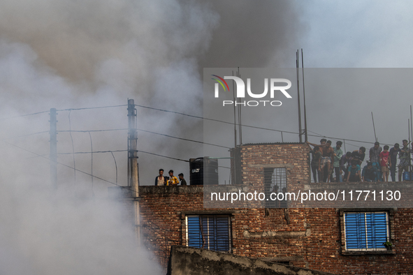 Smoke rises from a burning shoe factory as locals gather on the rooftop of a nearby building in a densely populated area of Dhaka, Banglades...