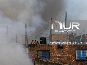 Smoke rises from a burning shoe factory as locals gather on the rooftop of a nearby building in a densely populated area of Dhaka, Banglades...