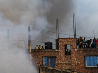 Smoke rises from a burning shoe factory as locals gather on the rooftop of a nearby building in a densely populated area of Dhaka, Banglades...