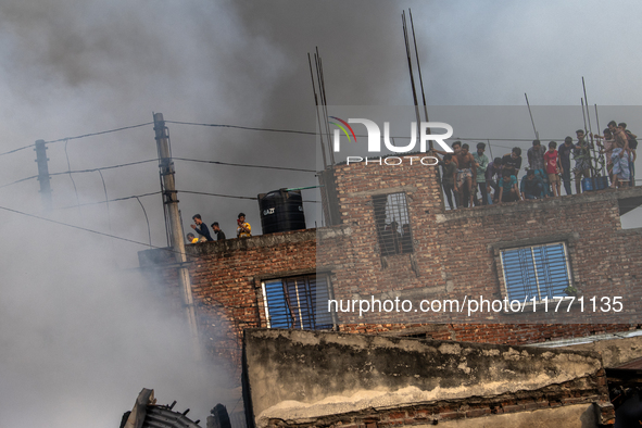 Smoke rises from a burning shoe factory as locals gather on the rooftop of a nearby building in a densely populated area of Dhaka, Banglades...