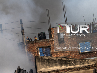 Smoke rises from a burning shoe factory as locals gather on the rooftop of a nearby building in a densely populated area of Dhaka, Banglades...