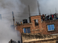 Smoke rises from a burning shoe factory as locals gather on the rooftop of a nearby building in a densely populated area of Dhaka, Banglades...