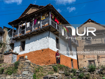 A woman stands in front of her traditional old home in the village of Makwanpur, Nepal, on November 12, 2024. (