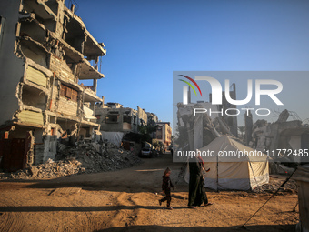 A Palestinian woman carries a child as they walk past the rubble of houses destroyed in previous strikes during the Israeli military offensi...