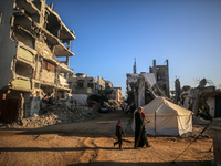 A Palestinian woman carries a child as they walk past the rubble of houses destroyed in previous strikes during the Israeli military offensi...