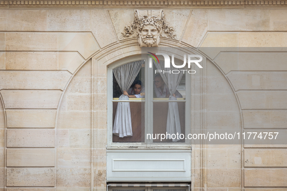 In Paris, France, on November 13, 2024, two members of the staff of the Elysee Palace pull back the curtains, peer through a window, and gaz...