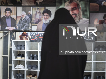 A veiled Iranian woman stands in front of a banner featuring portraits of Lebanon's Hezbollah leader, Hassan Nasrallah, who was killed in an...