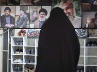 A veiled Iranian woman stands in front of a banner featuring portraits of Lebanon's Hezbollah leader, Hassan Nasrallah, who was killed in an...