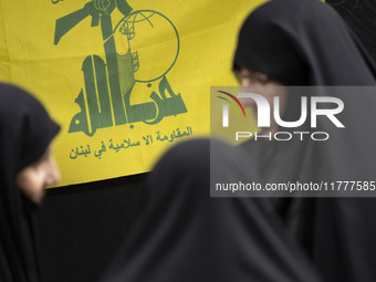 Veiled Iranian women talk to each other while standing in front of a flag of Lebanon's Hezbollah as they arrive to take part in a charity ce...