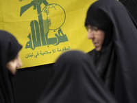 Veiled Iranian women talk to each other while standing in front of a flag of Lebanon's Hezbollah as they arrive to take part in a charity ce...