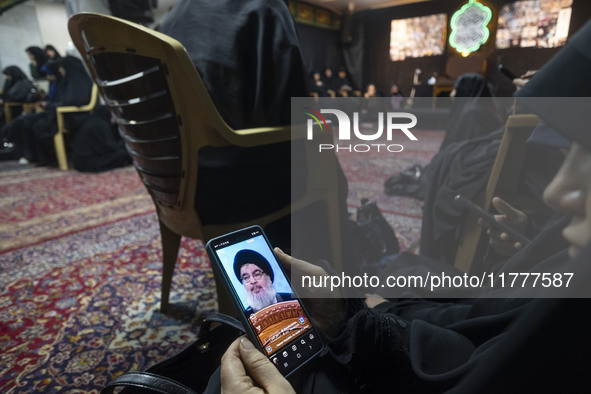 A veiled Iranian woman uses her cellphone featuring a portrait of Lebanon's Hezbollah leader, Hassan Nasrallah, in a suburb of Beirut, while...