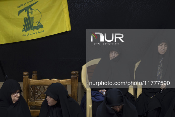 Veiled Iranian women sit together under a flag of Lebanon's Hezbollah while participating in a charity ceremony to donate gold and money to...