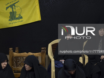 Veiled Iranian women sit together under a flag of Lebanon's Hezbollah while participating in a charity ceremony to donate gold and money to...