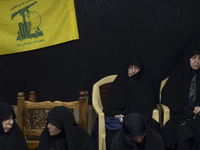 Veiled Iranian women sit together under a flag of Lebanon's Hezbollah while participating in a charity ceremony to donate gold and money to...