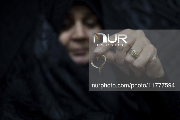 A veiled Iranian woman holds her gold necklace for a photograph while participating in a charity ceremony to donate gold and money to help t...