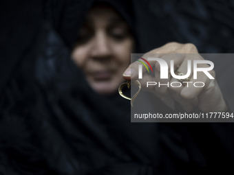 A veiled Iranian woman holds her gold necklace for a photograph while participating in a charity ceremony to donate gold and money to help t...