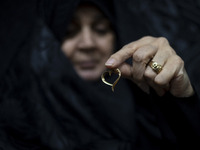 A veiled Iranian woman holds her gold necklace for a photograph while participating in a charity ceremony to donate gold and money to help t...