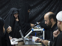 Two veiled Iranian women count donated Iranian banknotes during a charity ceremony to help the Lebanese Resistance Front and its affected pe...